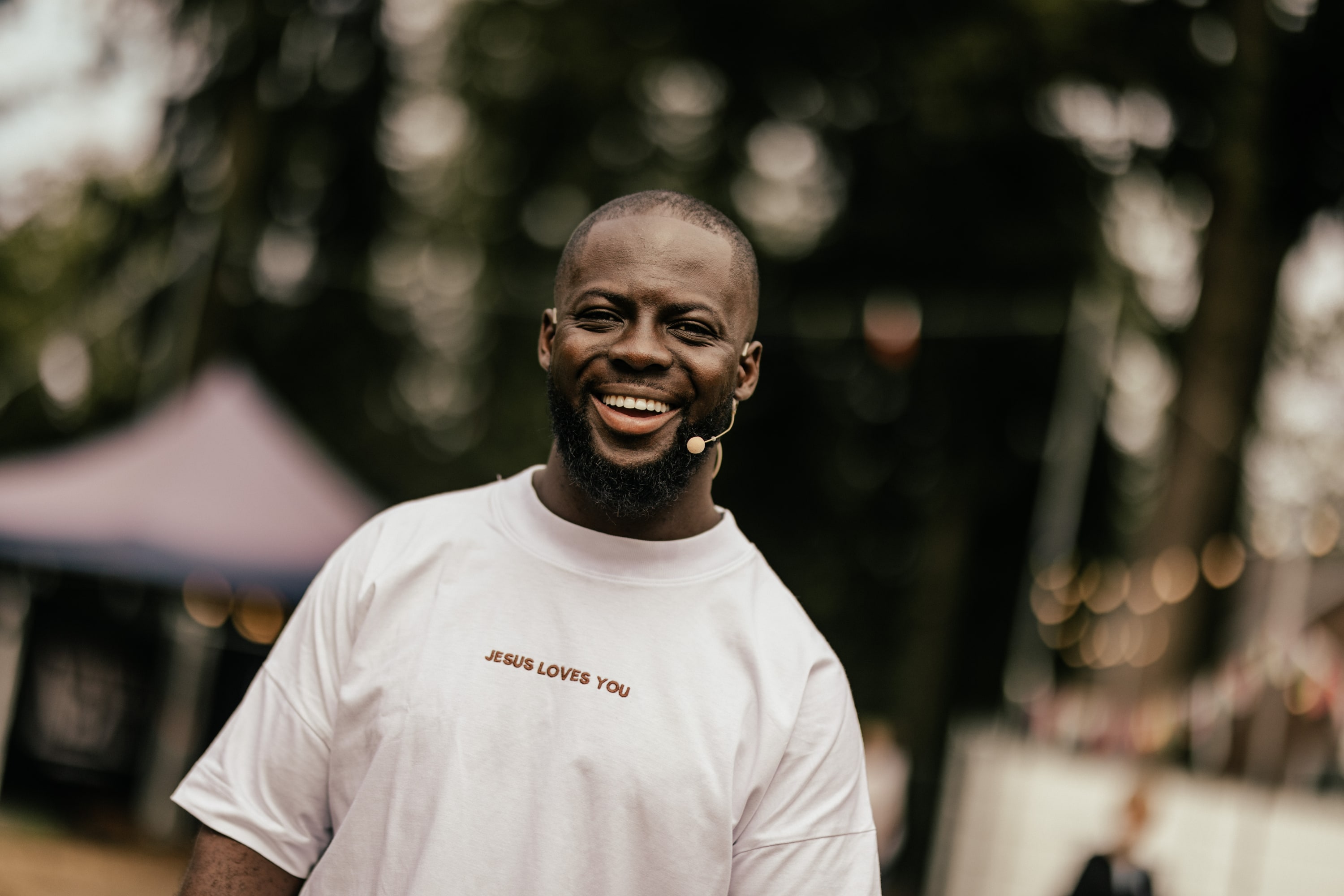 Close-up van een lachende Godwin Arhin met headsetmicrofoon op een festivalterrein
